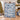 Yuletide Keepsake Patchwork woven blanket in blue held up beside a Christmas tree, blue and warm ivory patchwork with Santa, snowman and toy train
